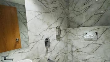 A bathroom with a marble wall, a sink, a toilet, and a shower.