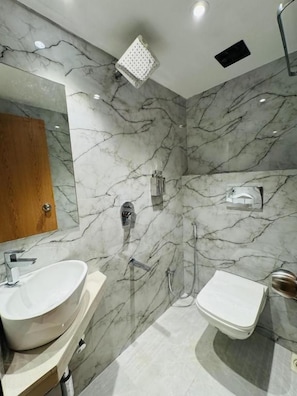 A bathroom with a marble wall, a sink, a toilet, and a shower. - Hotel Comfort Castle (Mumbai)