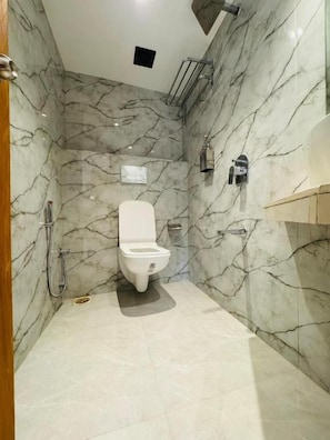 A bathroom with a toilet, a shower, and a marble wall. - Hotel Comfort Castle (Mumbai)