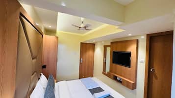A hotel room with a bed, a television mounted on the wall, and a ceiling fan.