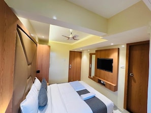 A hotel room with a bed, a television mounted on the wall, and a ceiling fan. - Hotel Comfort Castle (Mumbai)