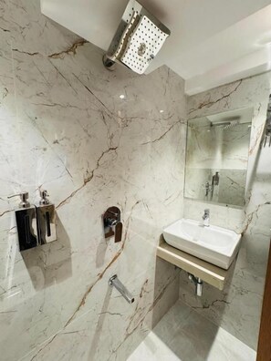 A modern bathroom with a marble floor, a built-in sink, a mirror, and a showerhead.