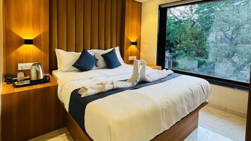 Een moderne slaapkamer met een houten hoofdbord, een groot bed met witte beddengoed en twee bedlampjes, met uitzicht op groen buiten.