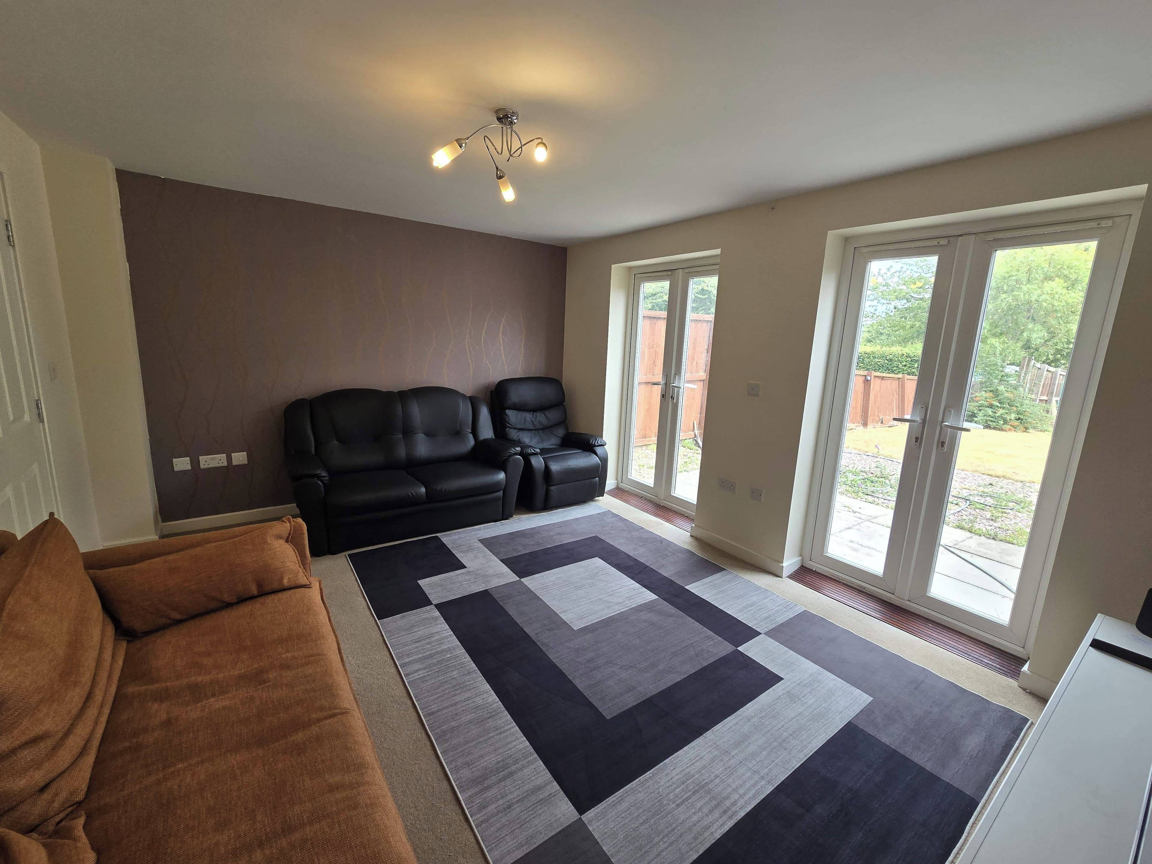 A living room with a sectional sofa, a patterned rug, and a ceiling light fixture.