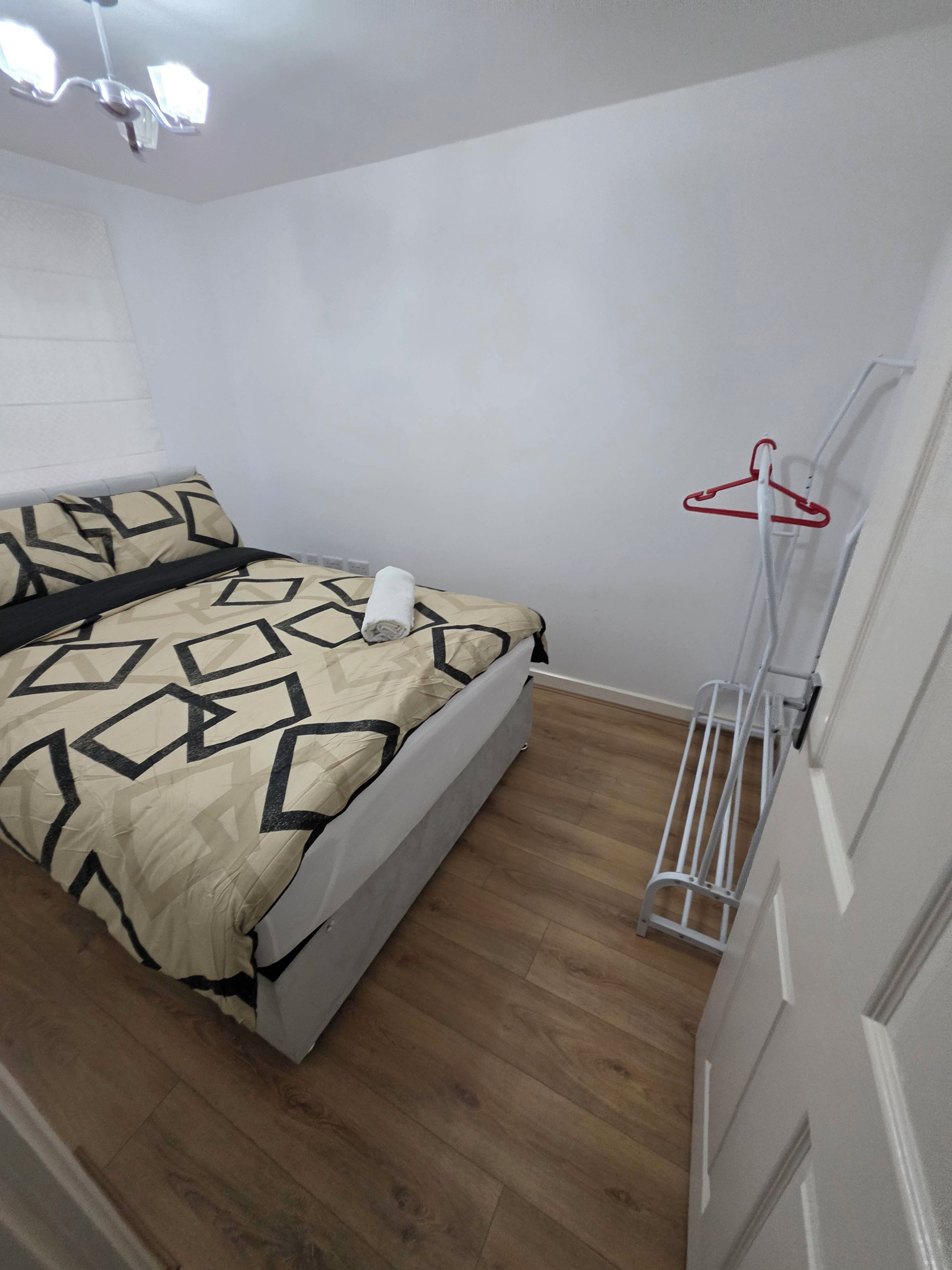 A bedroom with a bed, a hanging clothes rack, and a ceiling fan.