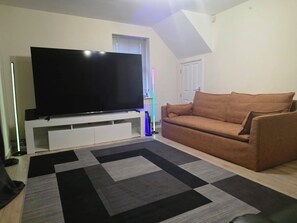 A living room with a flat-screen TV on a white stand, a brown sofa, and a patterned rug.