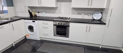 A modern kitchen with white cabinets, a gas stove, a built-in oven, and a washing machine.