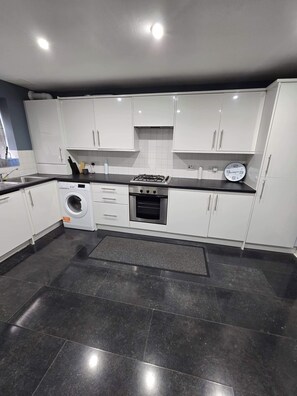 A modern kitchen with white cabinets, a gas stove, a built-in oven, and a washing machine.
