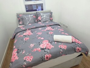 A bed with a floral bedspread, pillows, and a rolled white towel.