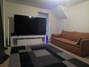 A living room with a flat-screen TV on a white entertainment unit, a brown sofa, and a patterned rug. - Shirebrook 2-bed Townhouse, With Free Parking, Ideal for Contractors and Families (Mansfield)