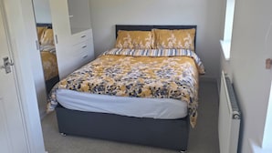 Ein Schlafzimmer mit Bett, Kleiderschrank, Deckenleuchte und Heizkörper.