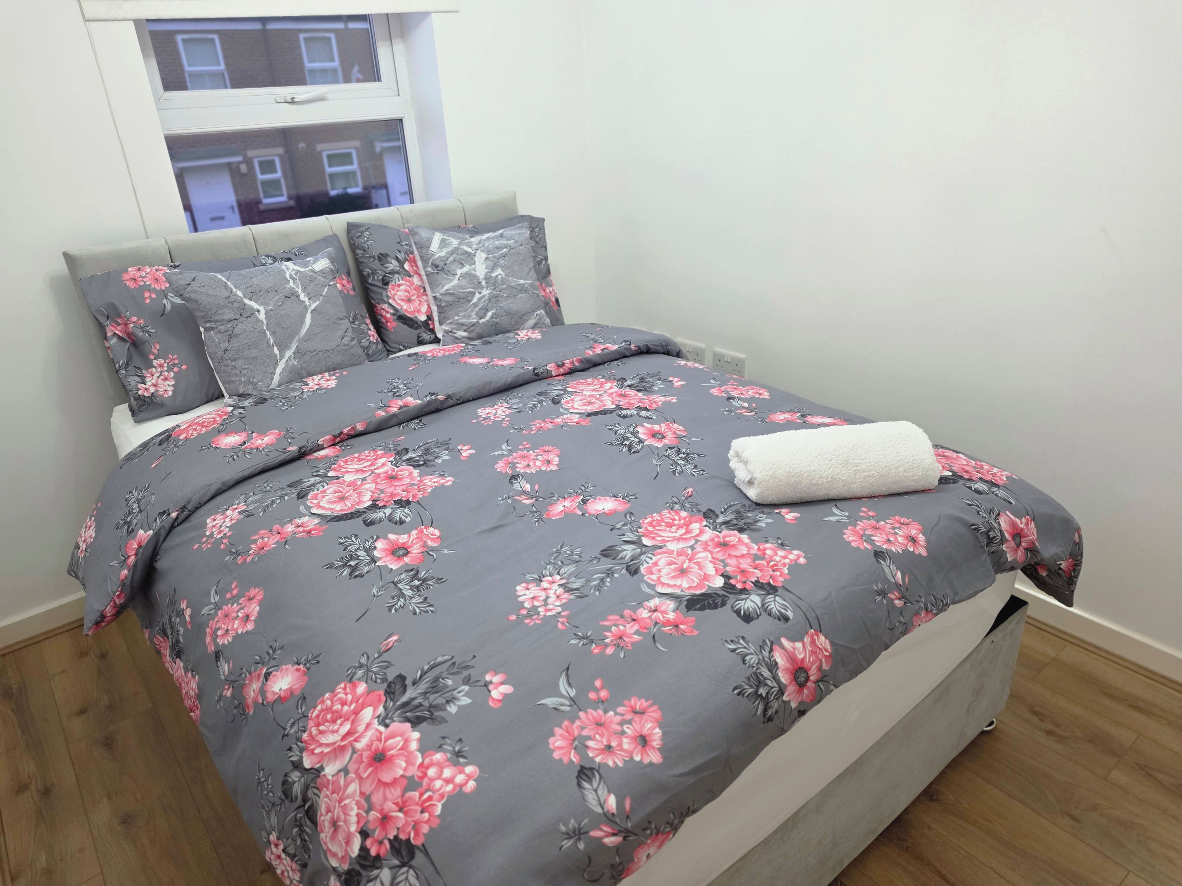 A bed with a floral bedspread, pillows, and a white towel.