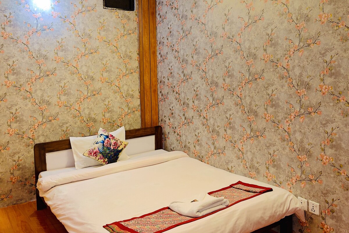 Ein Schlafzimmer mit einem Bett, Holzvertäfelung, einem Deckenventilator und floralem Wandpapier.