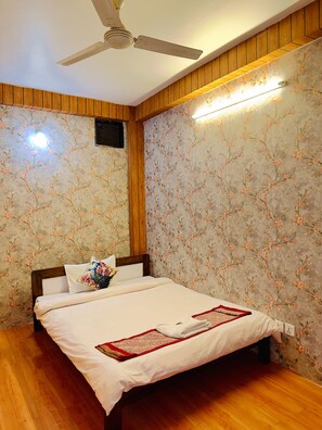 Ein Schlafzimmer mit einem Bett, Holzvertäfelung, einem Deckenventilator und floralem Wandpapier.
