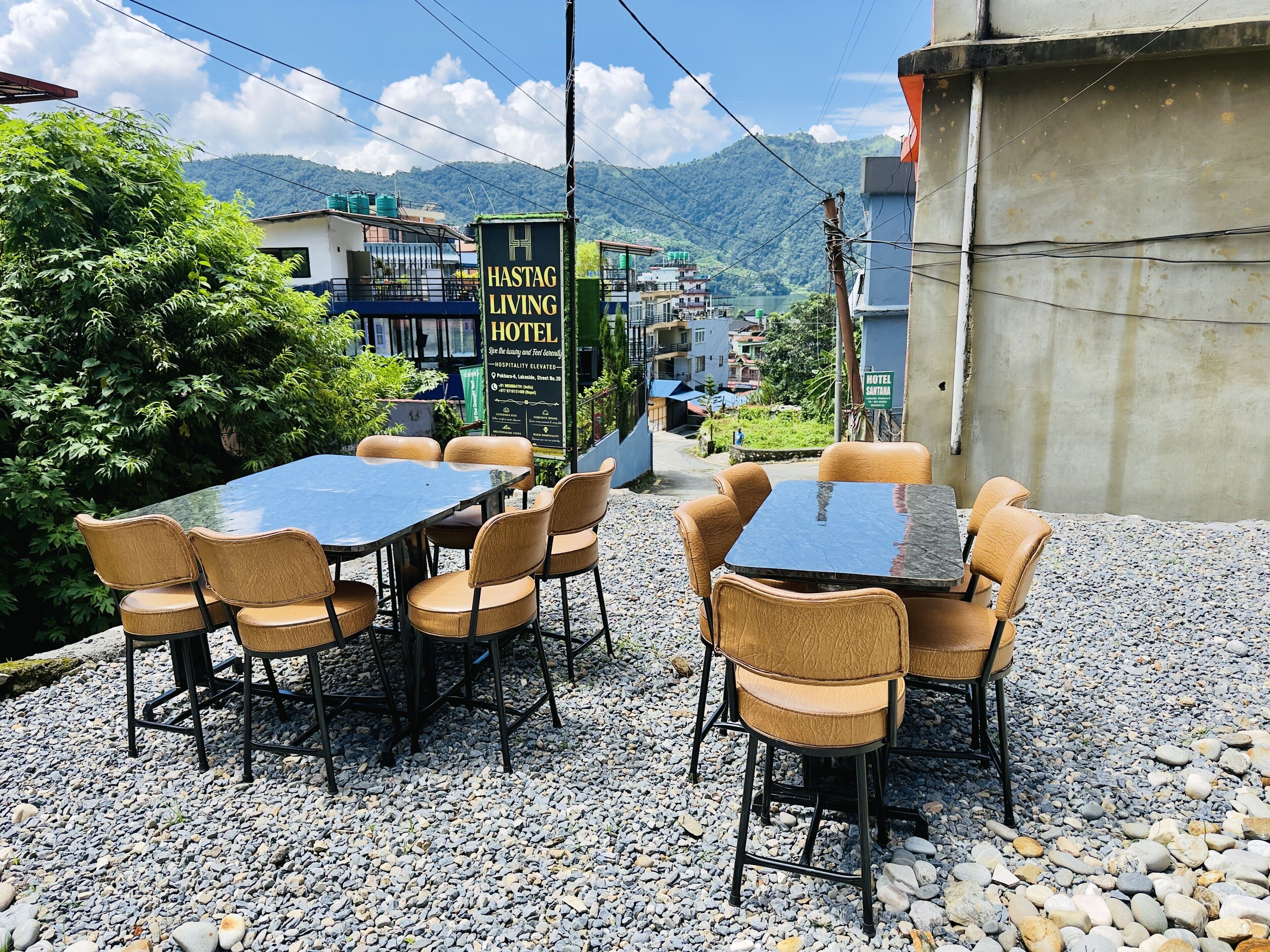 An outdoor seating area with tables and chairs, a sign for a hotel, and a view of a mountain.