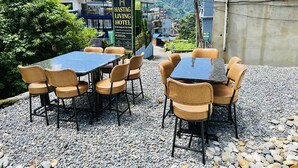 Un área exterior con mesas y sillas, un cartel de hotel y vistas a la montaña.