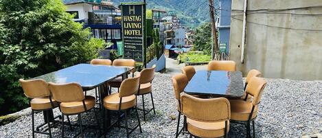 An outdoor seating area with tables and chairs, a sign for a hotel, and a view of a mountain.