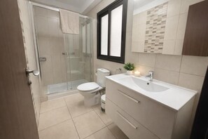 A modern bathroom with a glass shower enclosure, a toilet, a sink, and a mirror. - Apartamento Canarias (Los Cristianos)