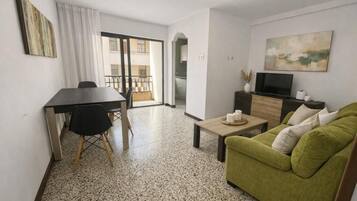 Una sala de estar con un sofá verde, una mesa de centro, un televisor y un comedor con mesa y sillas.