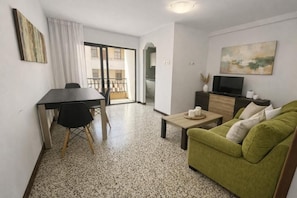 A living room with a green sofa, a coffee table, a TV, and a dining area with a table and chairs. - Apartamento Canarias (Los Cristianos)