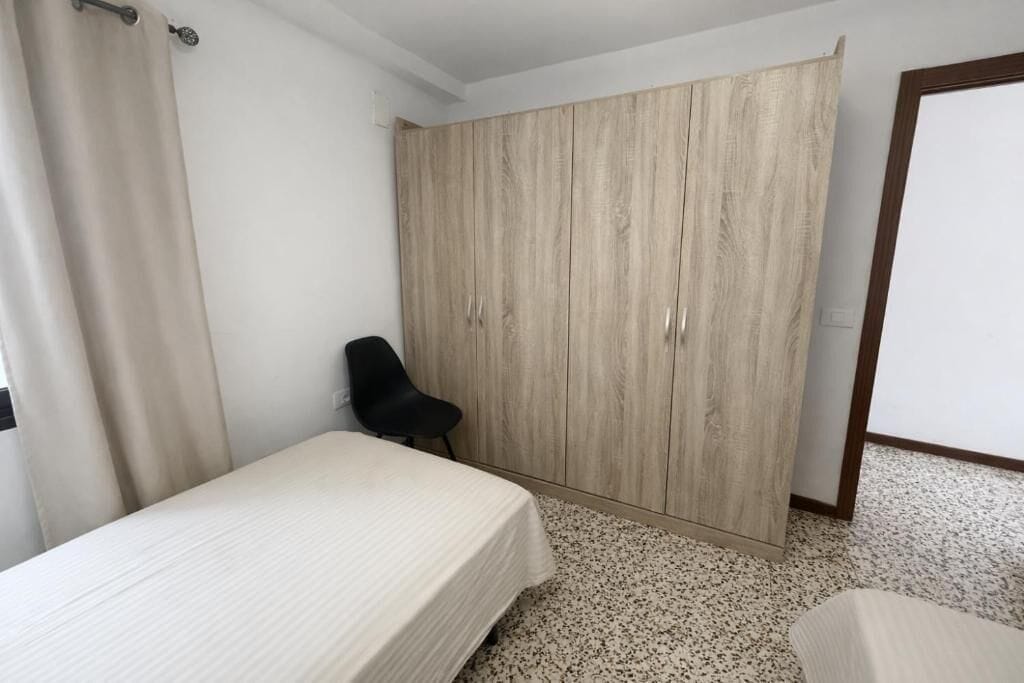 Un dormitori amb un llit, una cadira, un armari i una porta.