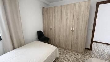 Un dormitori amb un llit, una cadira, un armari i una porta.