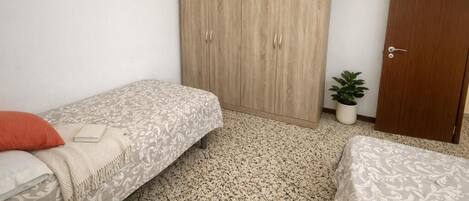 A bedroom with two single beds, a wardrobe, a potted plant, and a door.