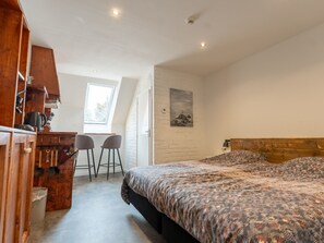 Une chambre à coucher avec un lit, un bureau, deux chaises, une fenêtre et un tableau accroché au mur.