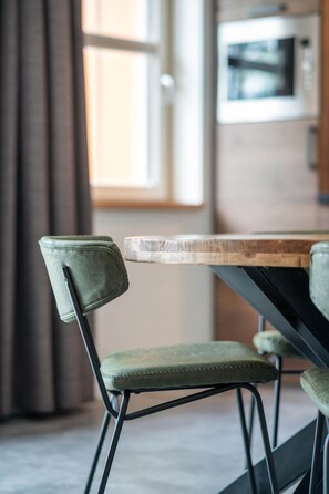 Un coin repas avec une table en bois et des chaises recouvertes d’un tissu vert.
