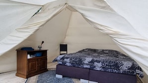 Eine Zelthütte mit einem Bett, einem kleinen Schrank und einem Teppich.