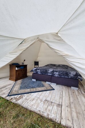 Un alloggio in tenda con un letto, un piccolo armadio e un tappeto.