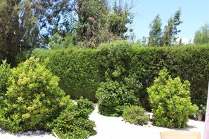 A well-maintained garden with various shrubs and trees, a gravel path, and a white building in the background. -  1-bedroom bungalow Limassol Countryside Tranquil Getaway Shared Pool Near Beach (Limassol)