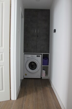 A laundry room with a washing machine, a cabinet, and a shelf with a purple container. -  1-bedroom bungalow Limassol Countryside Tranquil Getaway Shared Pool Near Beach (Limassol)