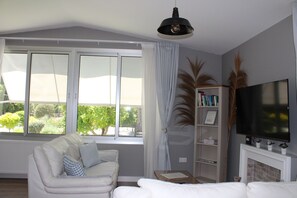 Una sala de estar con un sofá, un televisor, una estantería y una ventana con cortinas.