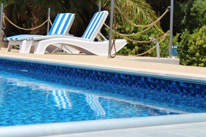 En swimmingpool med blå mosaikplattor, vita solstolar med blå ränder och ett avspärrningsrep.