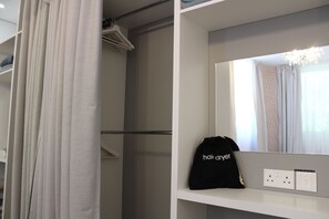Habitación de hotel con cortina de ducha blanca, espejo con luz superior y bolso negro con la etiqueta 'secador de pelo'.