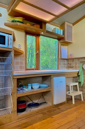 A compact kitchen with wooden cabinets, a built-in microwave, and a window overlooking greenery. - Camping Ont Moeten - Rumi by Interhome (Rekken)