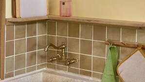 Eine Küche mit einer Holzarbeitsplatte, einem Spülbecken mit einem alten Wasserhahn und einem grünen Handtuch an einem Wäscheständer.