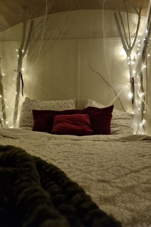 A bed with a patterned bedspread, two pillows, and a view of a room with wooden walls and branches with lights. - Camping Ont Moeten - T piept zo by Interhome (Rekken)