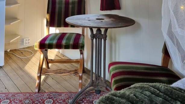 Une pièce chaleureuse avec un plafond en bois, une table ronde, une chaise à rayures et une fenêtre avec des rideaux.