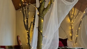 Ein Zimmer mit einem Bett, einem dekorativen Baum mit Lichtern und einem weißen Baldachin.