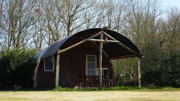 Eine rustikale Holzhütte mit großer Veranda und Metalldach, umgeben von Bäumen.