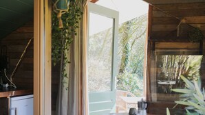 Ein Holzblockhaus-Innenraum mit Essbereich, einer Küche inklusive Kühlschrank und Blick auf den umliegenden Wald.