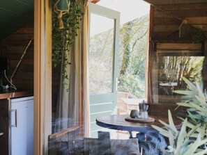 A wooden cabin interior with a dining area, a kitchen with a refrigerator, and a view of the surrounding forest. - Camping Ont Moeten - Waterflow by Interhome (Rekken)