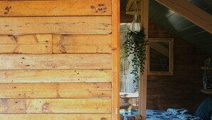 Ein Interieur einer Holzhütte mit einem Bett, einer hängenden Pflanze und einem Fenster.