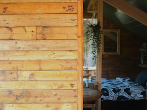 A wooden cabin interior with a bed, a hanging plant, and a window. - Camping Ont Moeten - Waterflow by Interhome (Rekken)