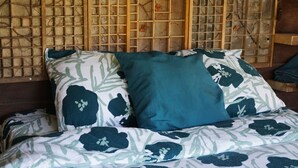 Ein Bett mit blumigem Bettbezug und zwei Kissen, eines türkis und eines dunkelblau, vor einer Wand mit Holzgittermuster.