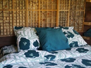 A bed with floral patterned bedding and two pillows, one teal and one dark blue, against a wall with a wooden lattice design. - Camping Ont Moeten - Waterflow by Interhome (Rekken)