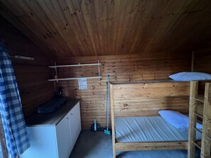 Pieni, puinen mökki, jossa on kerrossängyt, työpöytä ja hylly.