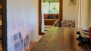 Ein Zimmer mit einem Holztisch, einem Bett mit Moskitonetz, einer Bank und einer hängenden Pflanze.